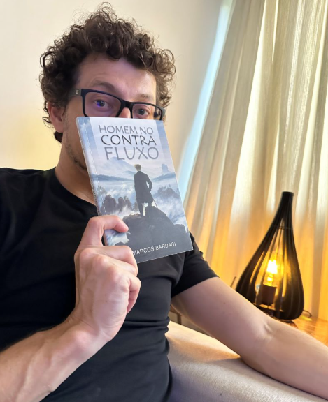 Cezar Cattani segurando o livro Homem no Contra Fluxo, de Marcos Bardagi